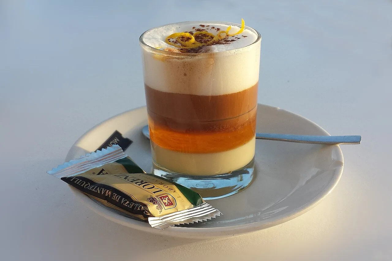Een gelaagde barraquito koffie in een klein glas met zichtbare lagen van gecondenseerde melk, Licor 43 en espresso op Tenerife