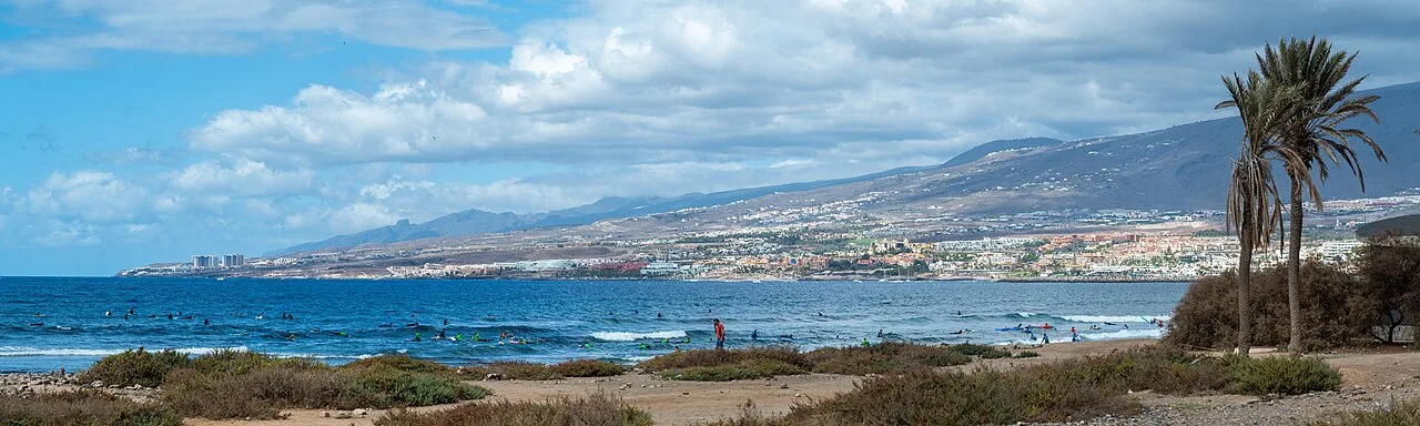 Panorama van de kust bij Playa de las Americas met surflessen en het strand van Playa del Duque op de achtergrond